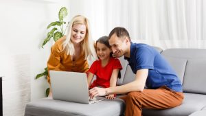 A family with a young child engaging with a laptop together in a bright living room.