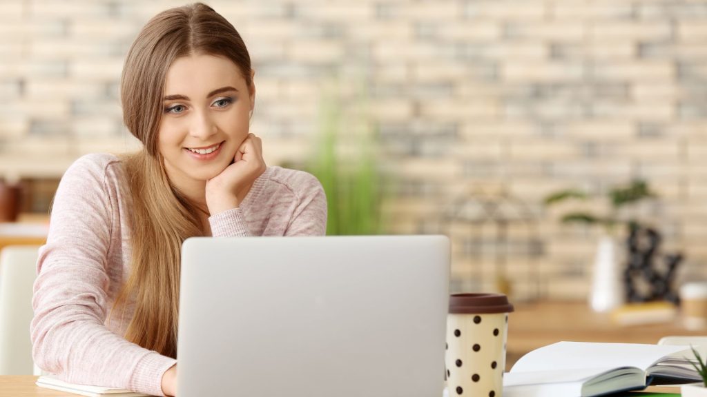 Young woman smiling at laptop screen in a bright room.